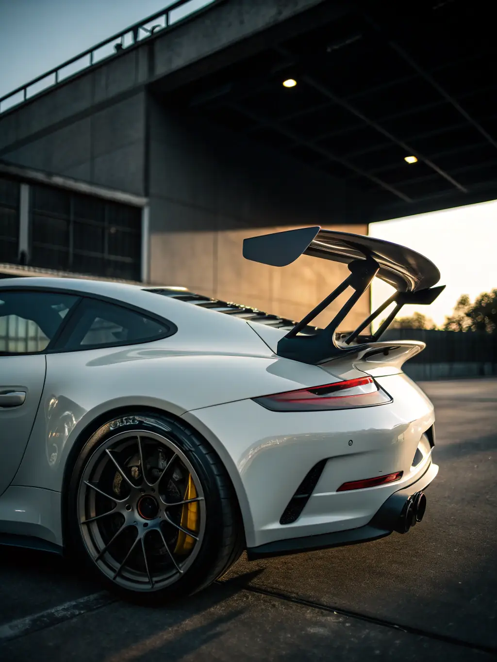 A sporty rear spoiler with a glossy finish and streamlined shape, designed to enhance a car's profile, displayed against a blurred background of a racetrack, emphasizing its aerodynamic benefits and stylish appearance.