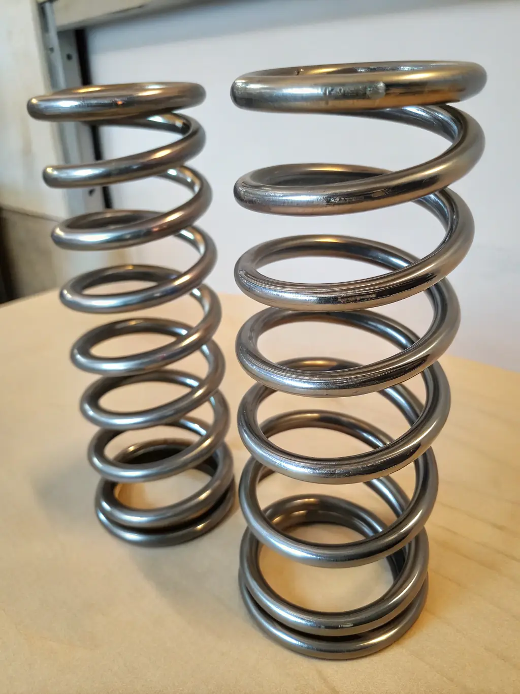 A suspension spring set featuring tightly wound coils with a glossy black finish, displayed on a clean surface with measuring tools nearby, emphasizing its strength, durability, and precision engineering.